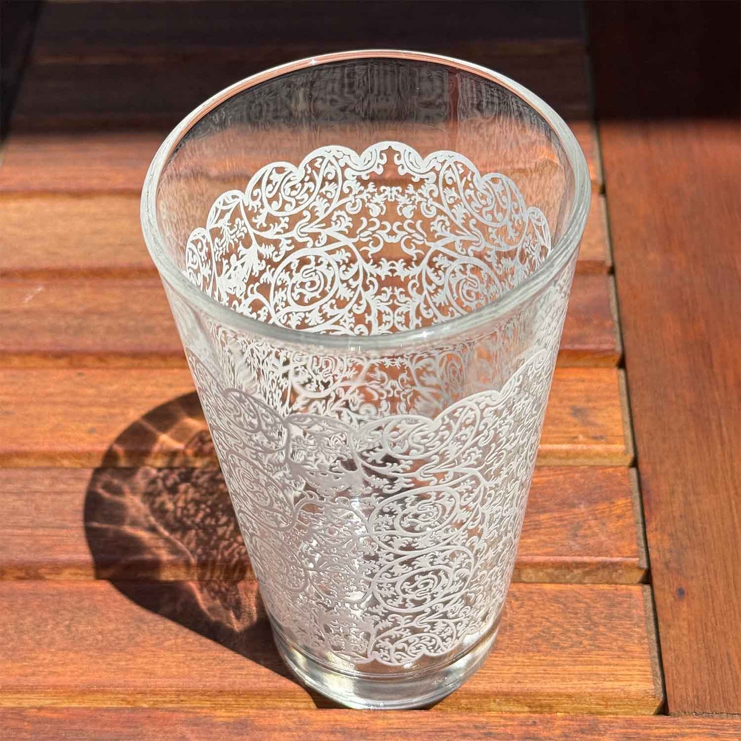 Water glass with intricate floral lace patterns on a wooden surface