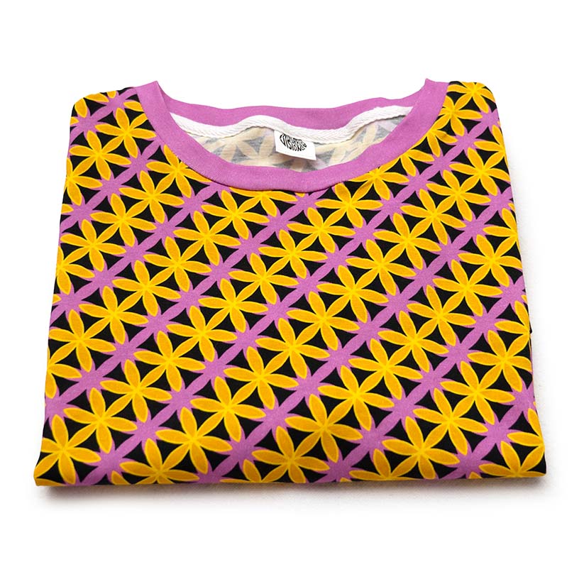 A folded short-sleeve crewneck shirt featuring a geometric pattern of yellow and pink flower-like shapes over a black background, with a solid pink collar.