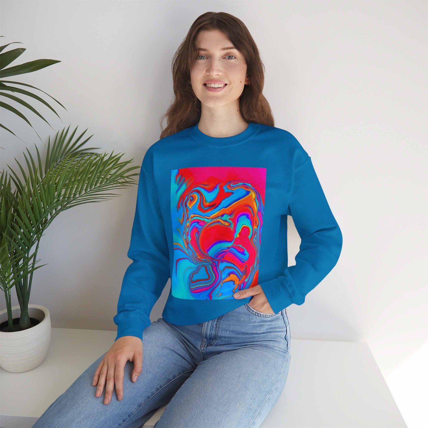 Person wearing a sapphire blue sweatshirt with a colorful abstract design, sitting in a room with a plant.