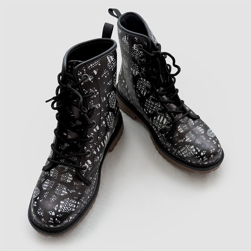 Angled view of black lace-up boots with black and white lace pattern on a white background