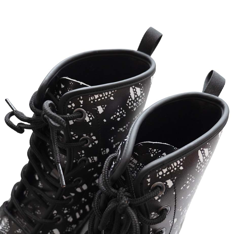 Top detail of black lace-up boots with black and white lace pattern on a white background