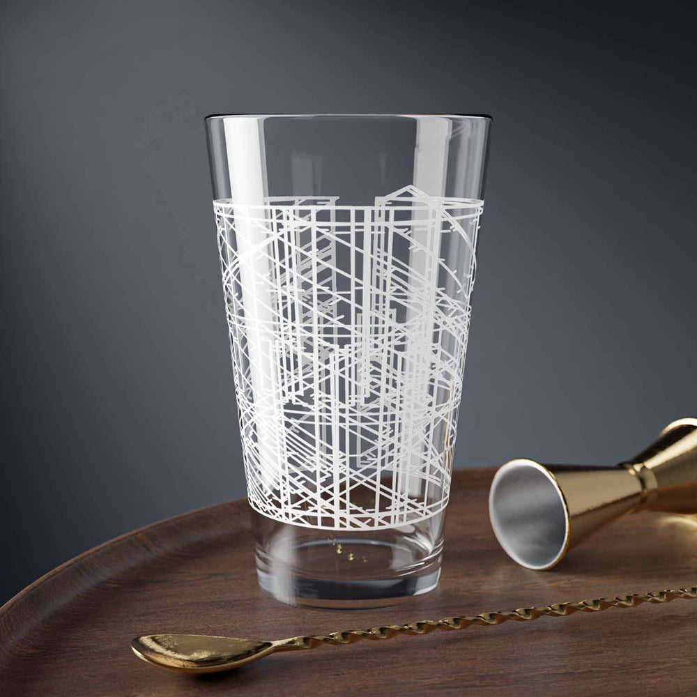 Clear glass with white geometric lines sitting on a wooden tray with a dark background with a spoon sitting next to it