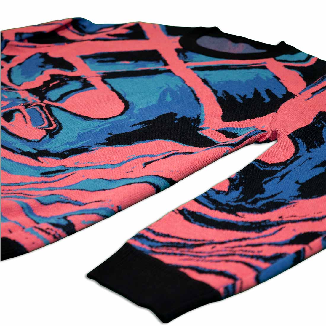 Knitted sweater with abstract design in pink, blue, and black laying flat at an angle on a white background