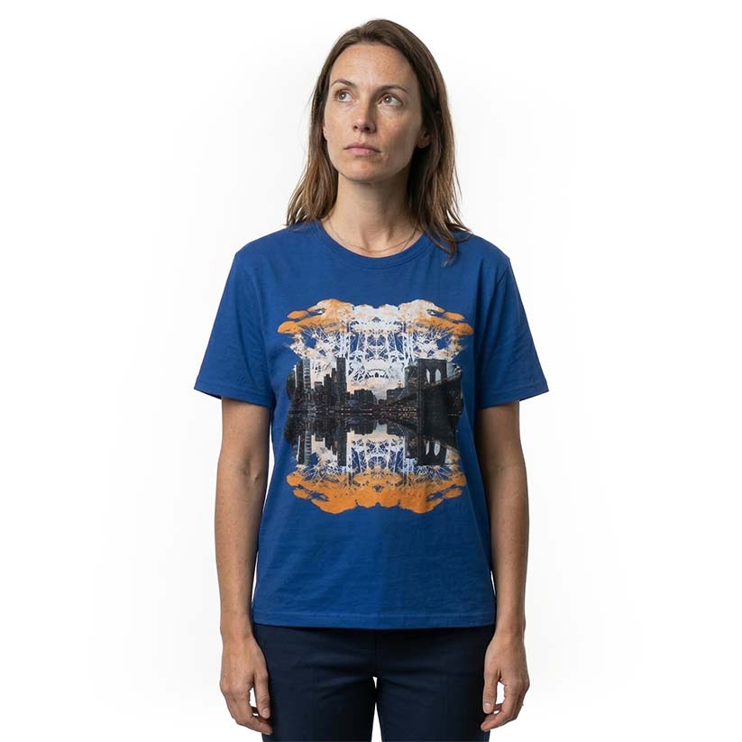 Woman wearing graphic print of trees and NYC skyline on a royal blue t-shirt on a white background